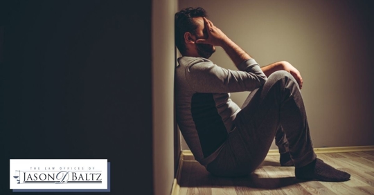 White man with hand on his head sitting down against a wall